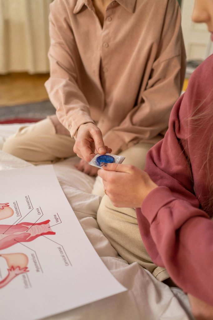 Close-up of a mother and daughter discussing sex education while holding a condom and studying anatomical diagrams.